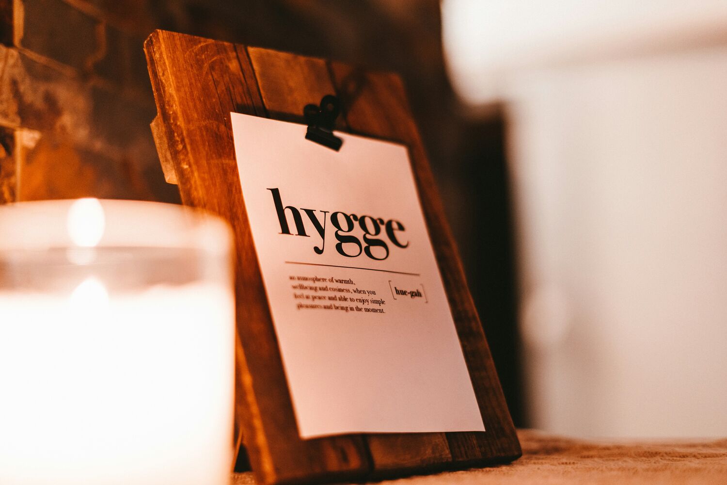 A lit candle beside a card reading hygge, with soft greenery
